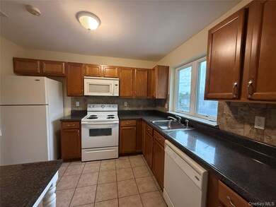 Kitchen with tasteful backsplash, white appliances, brown cabinets, and light tile patterned flooring
