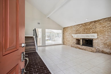 Step into the formal living room featuring accent brick accent wall, soaring ceiling, gas log fireplace, and neutral tile flooring.