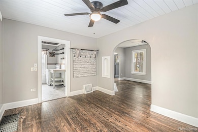 Unfurnished room featuring arched walkways, dark wood finished floors, ceiling fan, and wooden ceiling