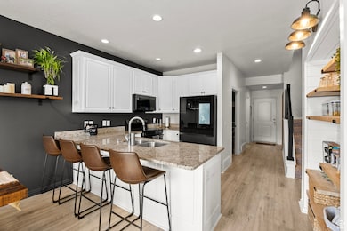 Kitchen with black appliances, open shelves, a peninsula, white cabinets, and light wood-style floors