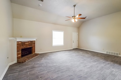 Unfurnished living room with a ceiling fan, lofted ceiling, a brick fireplace, and wood finished floors