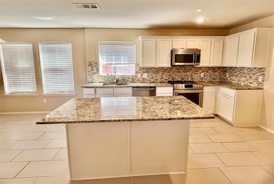 Kitchen with white cabinetry, tasteful backsplash, light stone countertops, and appliances with stainless steel finishes