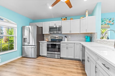 Kitchen featuring appliances with stainless steel finishes, light stone counters, decorative backsplash, white cabinetry, and light wood finished floors