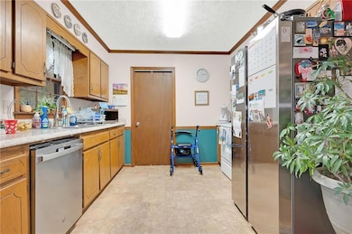 Kitchen with appliances with stainless steel finishes, a textured ceiling, light countertops, crown molding, and brown cabinetry