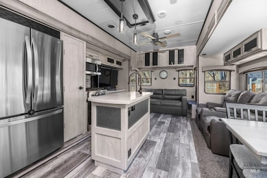 Kitchen with stainless steel appliances, an island with sink, dark wood-type flooring, and light brown cabinetry