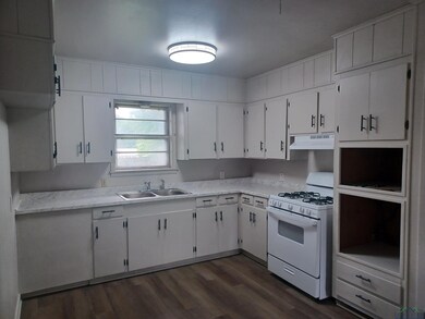 Kitchen featuring white gas stove, a sink, under cabinet range hood, light countertops, and dark wood finished floors
