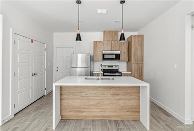 Kitchen featuring hanging light fixtures, light hardwood / wood-style floors, appliances with stainless steel finishes, sink, and a kitchen island with sink