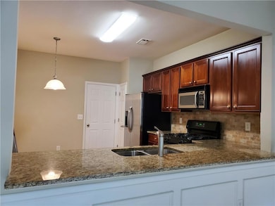 Kitchen with appliances with stainless steel finishes, stone counters, backsplash, pendant lighting, and a peninsula