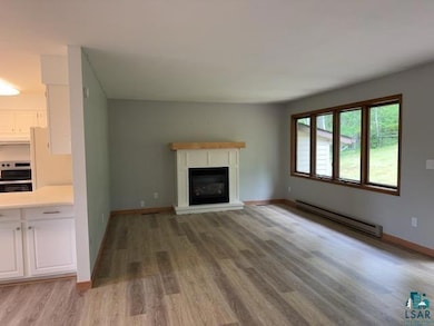 Unfurnished living room featuring baseboard heating, wood finished floors, and a glass covered fireplace