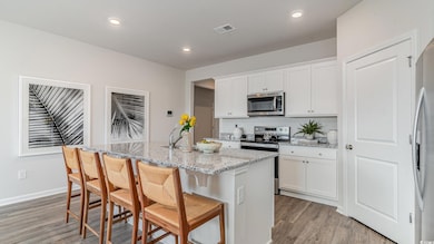 Kitchen featuring stainless steel appliances, light wood-type flooring, an island with sink, white cabinetry, and light stone counters