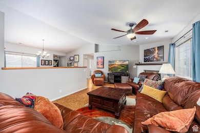 Living room with a fireplace, lofted ceiling, a chandelier, and a ceiling fan