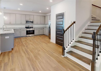 Kitchen featuring stainless steel appliances, sink, light hardwood / wood-style floors, gray cabinets, and pendant lighting