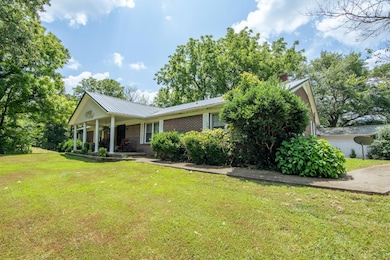 View of front of property featuring a front lawn, brick siding, a metal roof, a porch, and a chimney