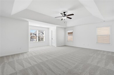 Empty room featuring a tray ceiling, light colored carpet, and a ceiling fan