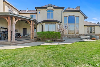 Rear view of property with a ceiling fan, stone siding, a lawn, a patio, and stucco siding