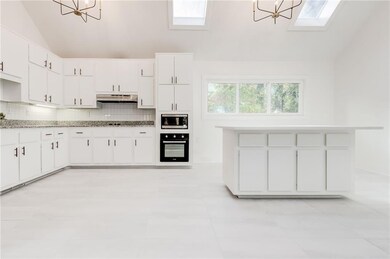 Main floor kitchen featuring oven, white cabinetry, hanging light fixtures, and a skylight