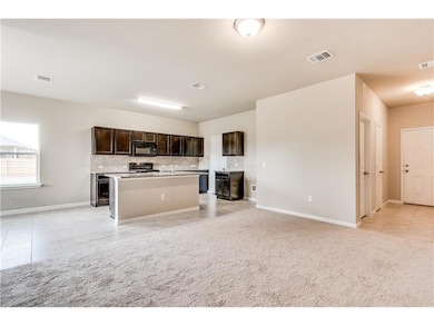 Kitchen with light tile patterned floors, a center island with sink, backsplash, and dark brown cabinets