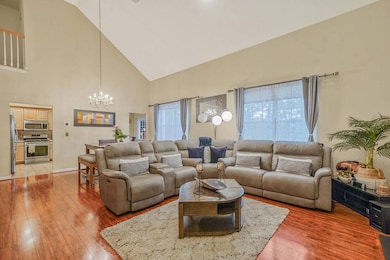 Living room featuring a chandelier, high vaulted ceiling, light wood finished floors, and baseboards