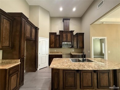 Kitchen with a center island with sink, stainless steel microwave, dark brown cabinets, and light stone countertops