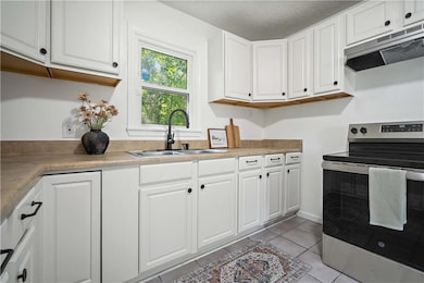 Kitchen with stainless steel range with electric stovetop, exhaust hood, white cabinets, light tile patterned flooring, and a textured ceiling