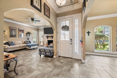 Foyer with crown molding, arched walkways, ceiling fan, a stone fireplace, and light tile patterned floors