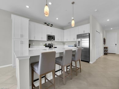 Kitchen featuring stainless steel appliances, light countertops, white cabinetry, a kitchen island with sink, and hanging light fixtures