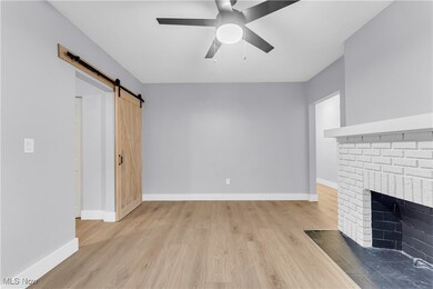 Unfurnished living room with light wood finished floors, a barn door, ceiling fan, and a brick fireplace
