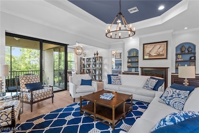 Living room featuring a raised ceiling, a fireplace, wood finished floors, a chandelier, and crown molding