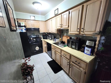Kitchen with light countertops, black appliances, light tile patterned floors, crown molding, and tasteful backsplash