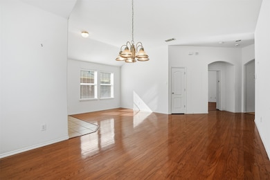 Unfurnished living room with a chandelier, arched walkways, and wood finished floors