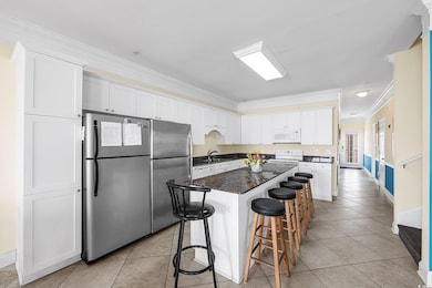 Kitchen featuring white appliances, crown molding, a breakfast bar, white cabinets, and light tile patterned flooring