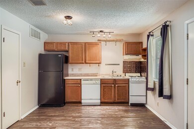 Kitchen featuring white appliances, dark wood-style flooring, light countertops, a textured ceiling, and under cabinet range hood