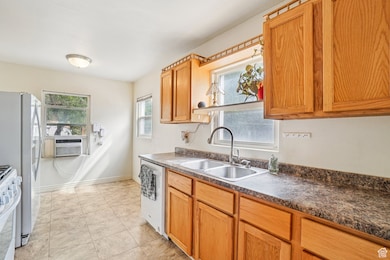 Kitchen featuring light tile patterned flooring, white appliances, dark countertops, brown cabinets, and cooling unit