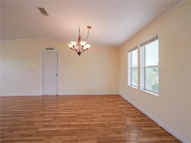 Empty room featuring crown molding, a chandelier, light wood finished floors, and vaulted ceiling