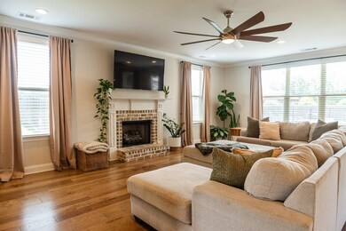 Living area featuring a ceiling fan, ornamental molding, baseboards, wood-type flooring, and a brick fireplace