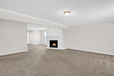 Unfurnished living room featuring carpet flooring, crown molding, and a lit fireplace