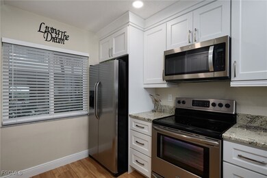 Kitchen with stainless steel appliances, white cabinets, light wood-type flooring, and light stone countertops