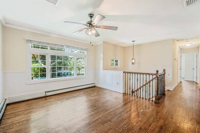 Spare room with wood finished floors, wainscoting, a ceiling fan, baseboard heating, and crown molding
