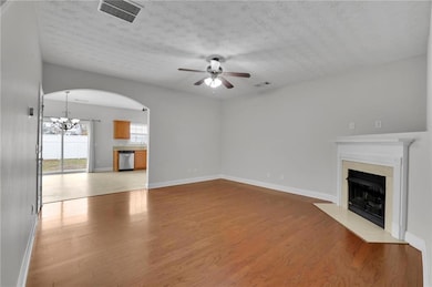 Unfurnished living room with light wood-style floors, a chandelier, ceiling fan, a fireplace, and arched walkways