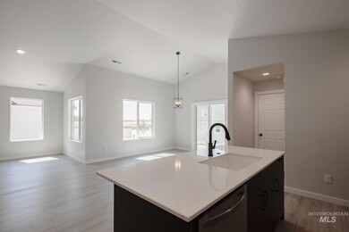 Kitchen featuring vaulted ceiling, light wood finished floors, dark cabinetry, dishwasher, and a kitchen island with sink