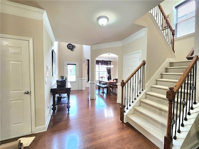 Foyer entrance featuring ornamental molding, stairway, arched walkways, dark wood-style floors, and a chandelier