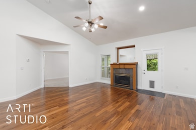 Unfurnished living room featuring dark wood-style floors, a tiled fireplace, vaulted ceiling, plenty of natural light, and recessed lighting