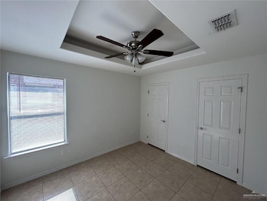 Unfurnished bedroom featuring a tray ceiling, light tile patterned floors, and ceiling fan