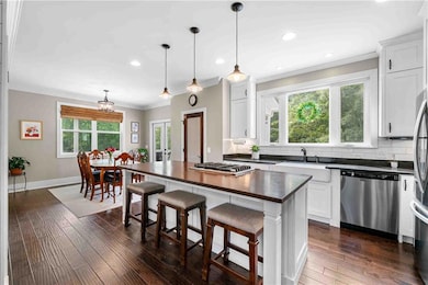 Kitchen with crown molding, stainless steel appliances, backsplash, white cabinets, and a breakfast bar area