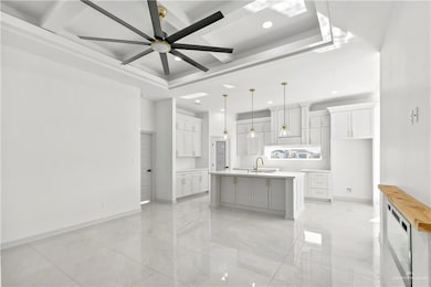 Kitchen featuring pendant lighting, sink, ceiling fan, an island with sink, and white cabinetry