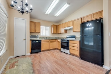 Kitchen with black appliances, a chandelier, vaulted ceiling, light wood-type flooring, and under cabinet range hood