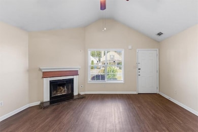 Unfurnished living room featuring dark wood-type flooring, ceiling fan, vaulted ceiling, and a fireplace with raised hearth