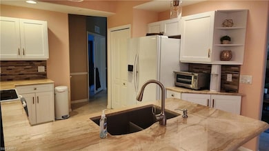 Kitchen with tasteful backsplash, white cabinetry, white appliances, open shelves, and light stone counters