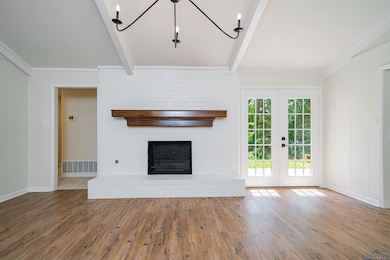 Unfurnished living room featuring beam ceiling, wood finished floors, a brick fireplace, and french doors