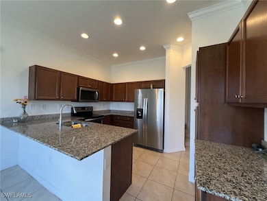 Kitchen with stainless steel appliances, dark stone counters, ornamental molding, light tile patterned floors, and a peninsula
